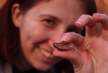 A woman smiling, holding a small brown rock cresent that looks like a grin.