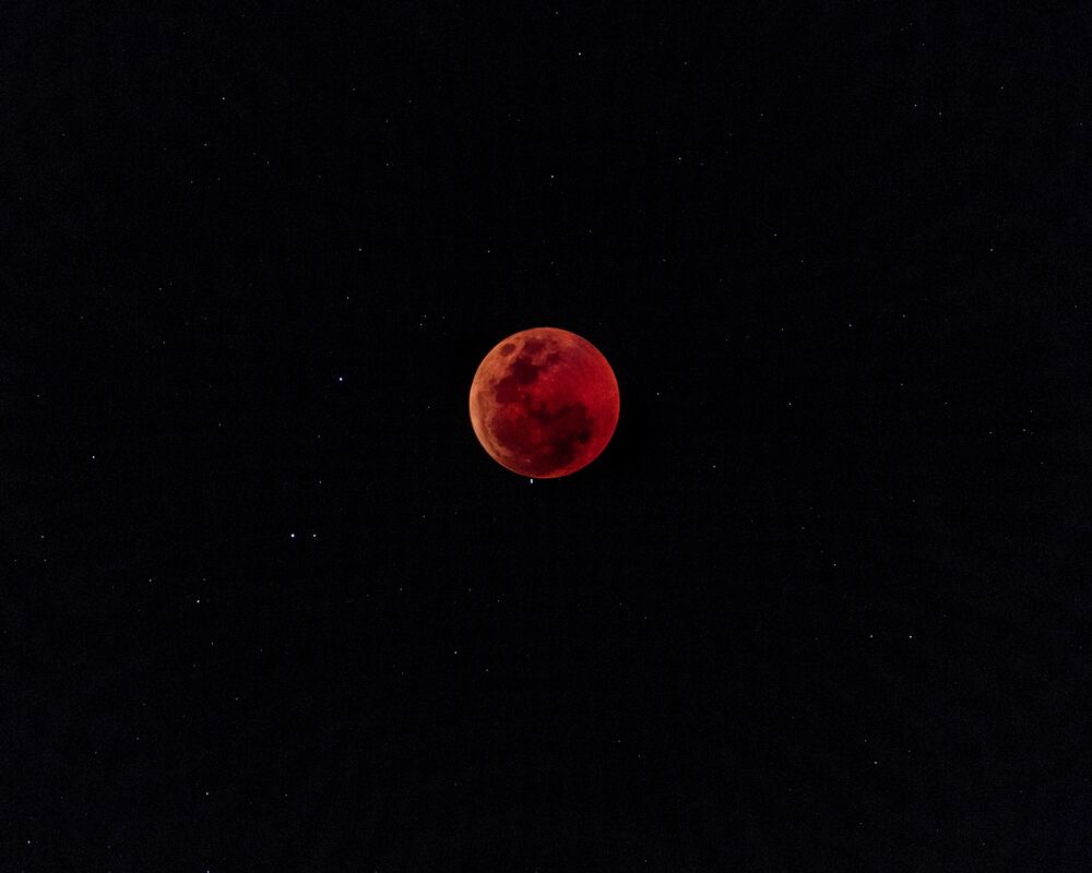 Blood-red moon hanging in night sky with stars.