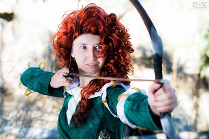 A red-haired woman in a green dress, preparing to loose an arrow from a bow.
